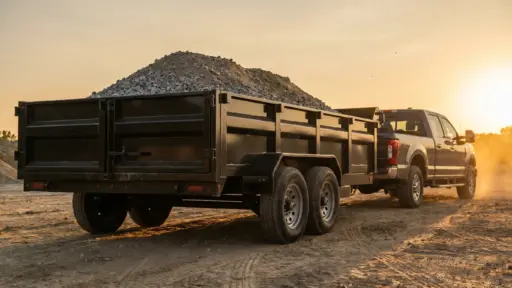 Black pickup truck with a loaded dump trailer on a dirt road at sunset