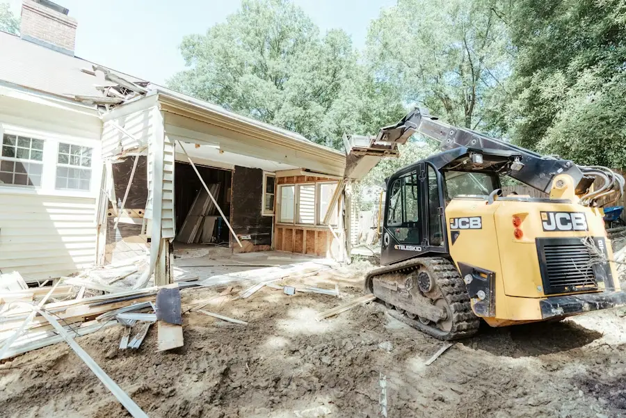Excavator demolishing a house exterior in a residential area under clear skies