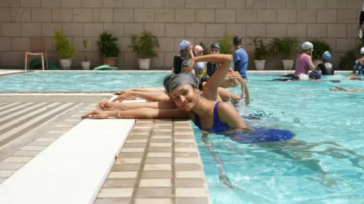 Group of women practicing swimming strokes in an outdoor pool with potted plants nearby