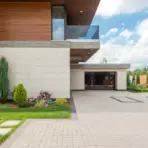 Modern house exterior with wooden accents, spacious driveway, and landscaped garden under a blue sky