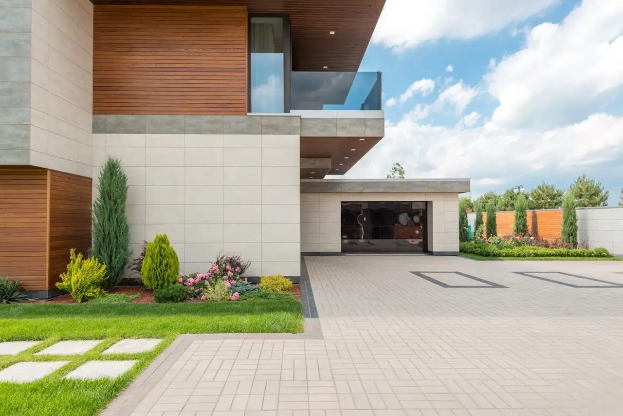 Modern house exterior with wooden accents, spacious driveway, and landscaped garden under a blue sky