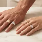 Hands wearing gold and silver signet rings resting on a marble surface