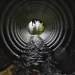 Flowing water inside large metal culvert leading to misty forest view