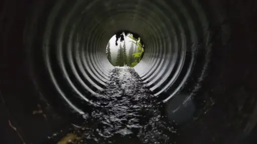 Flowing water inside large metal culvert leading to misty forest view