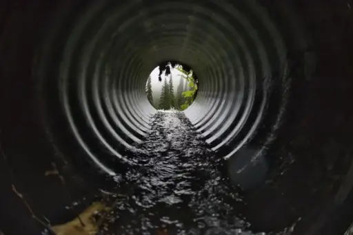 Flowing water inside large metal culvert leading to misty forest view