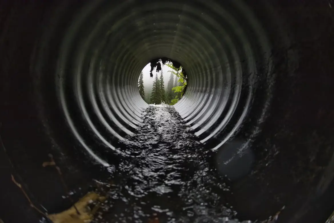 Flowing water inside large metal culvert leading to misty forest view