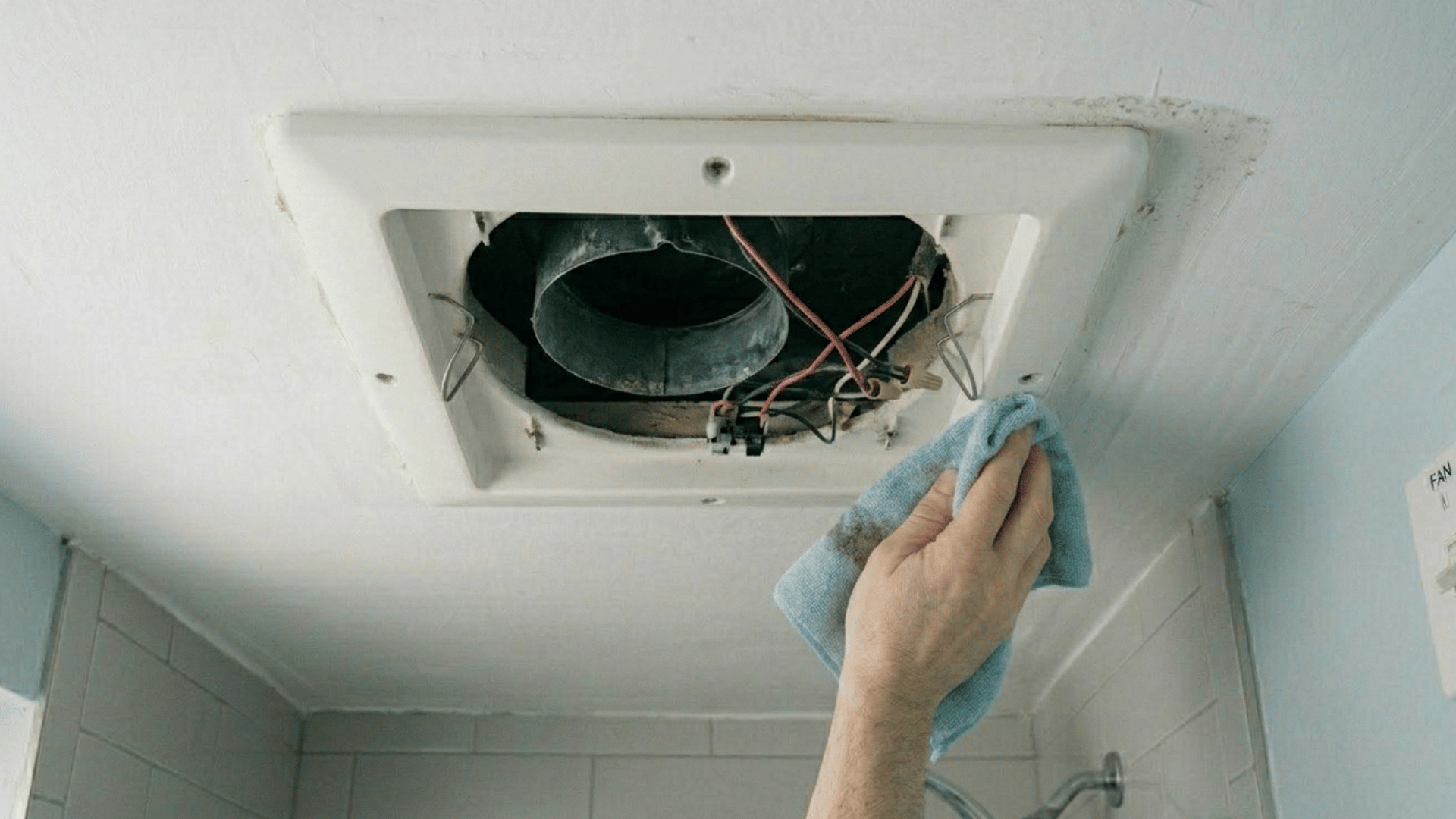 wiping inside of bathroom exhaust fan housing with cloth.