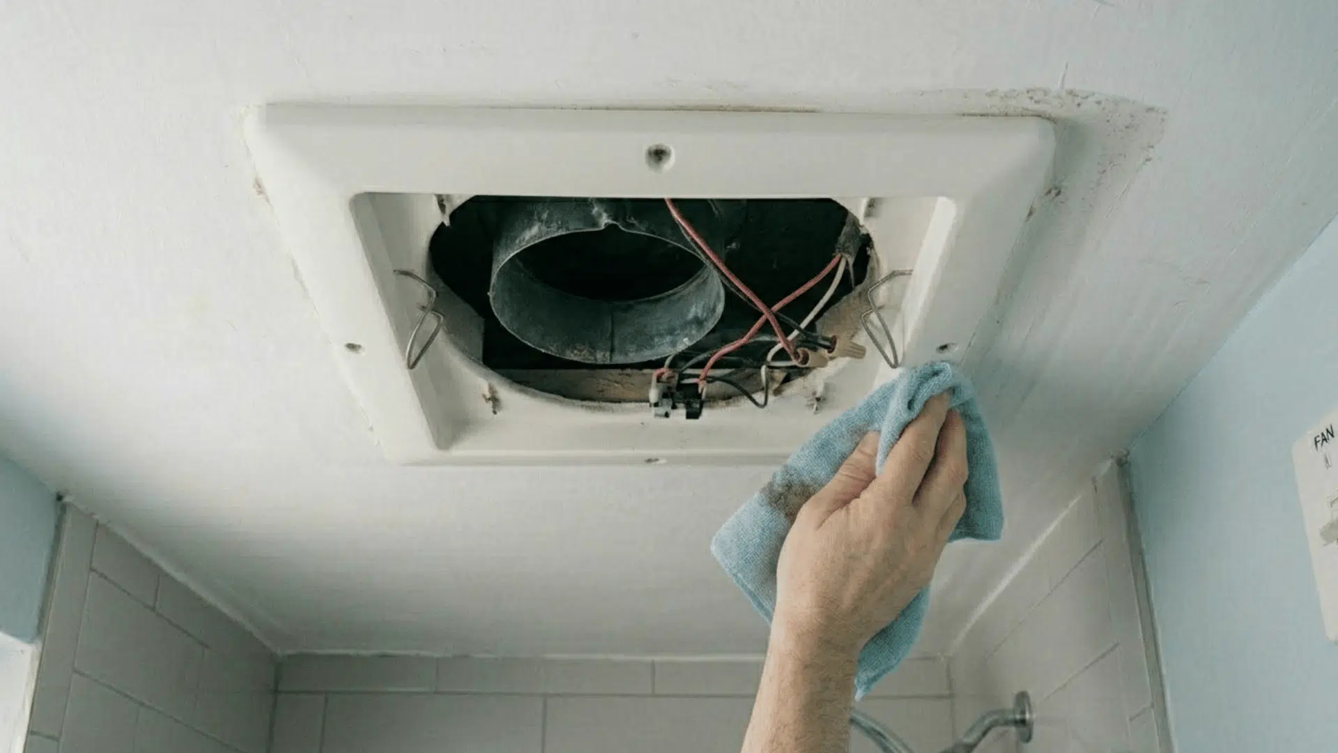 wiping inside of bathroom exhaust fan housing with cloth.