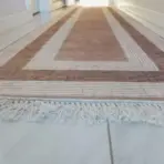 Geometric-patterned hallway runner rug with fringed edges on white tiled floor