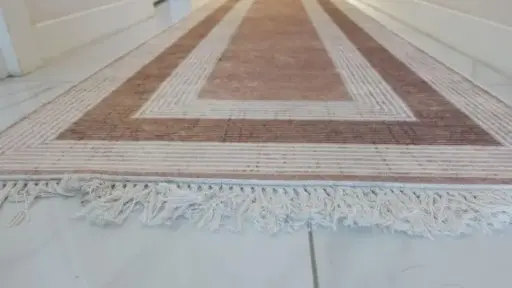 Geometric-patterned hallway runner rug with fringed edges on white tiled floor
