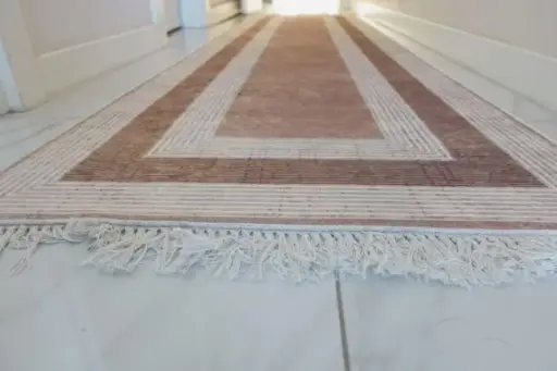 Geometric-patterned hallway runner rug with fringed edges on white tiled floor