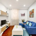 Cozy living room with blue sofa, white coffee table, and TV stand in bright natural light