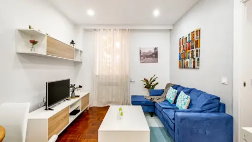 Cozy living room with blue sofa, white coffee table, and TV stand in bright natural light