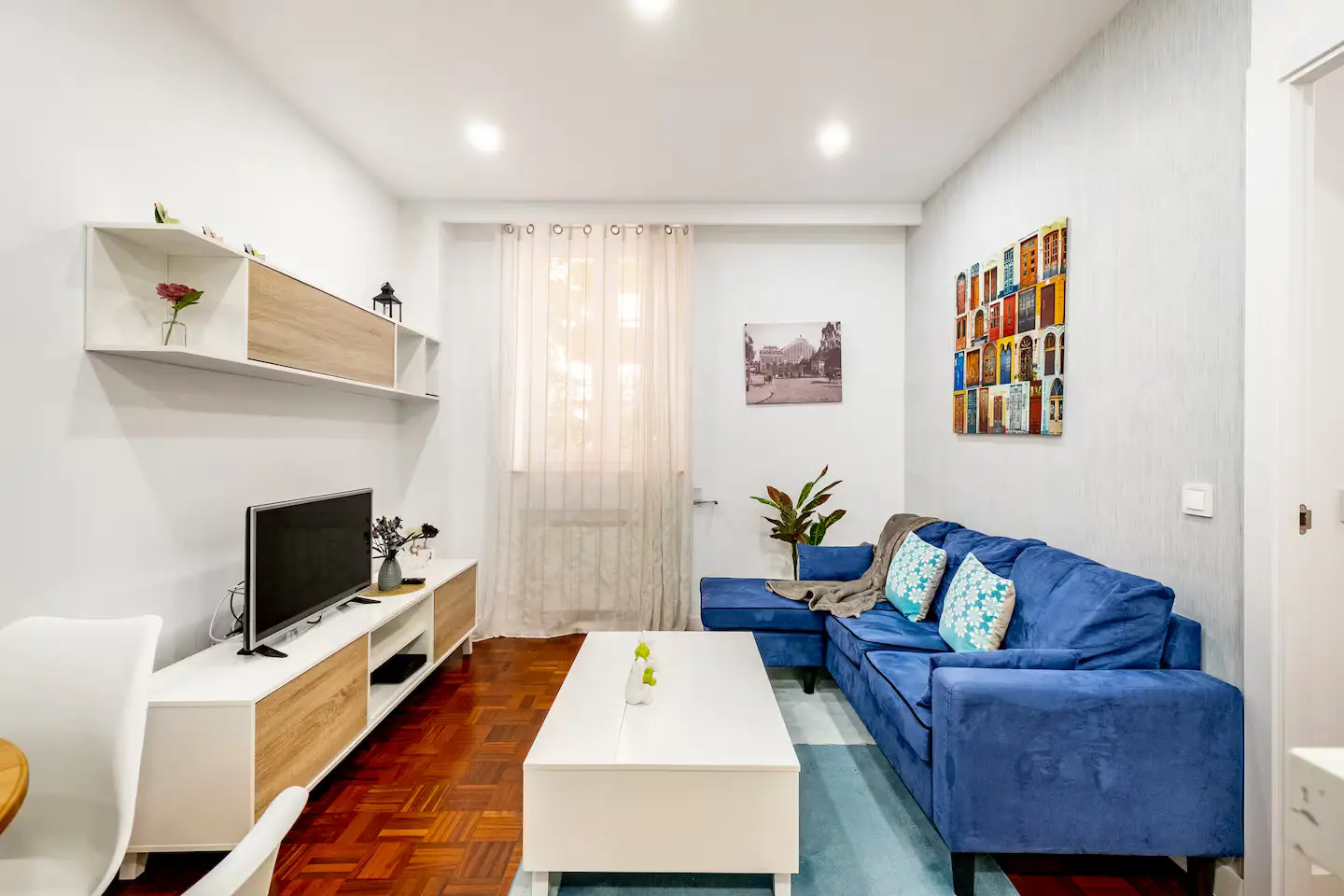 Cozy living room with blue sofa, white coffee table, and TV stand in bright natural light