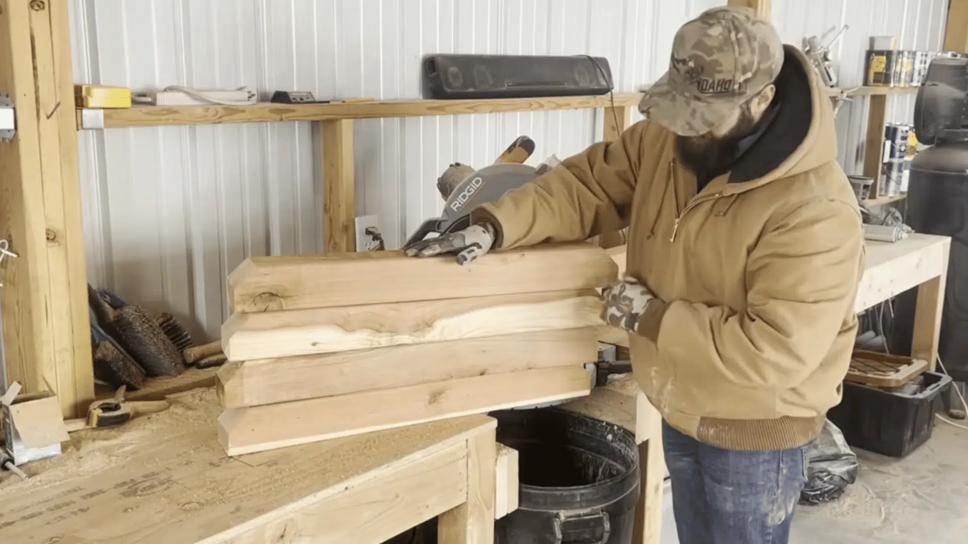 a bearded man in a workshop stacking and inspecting wooden beams on a workbench surrounded by tools