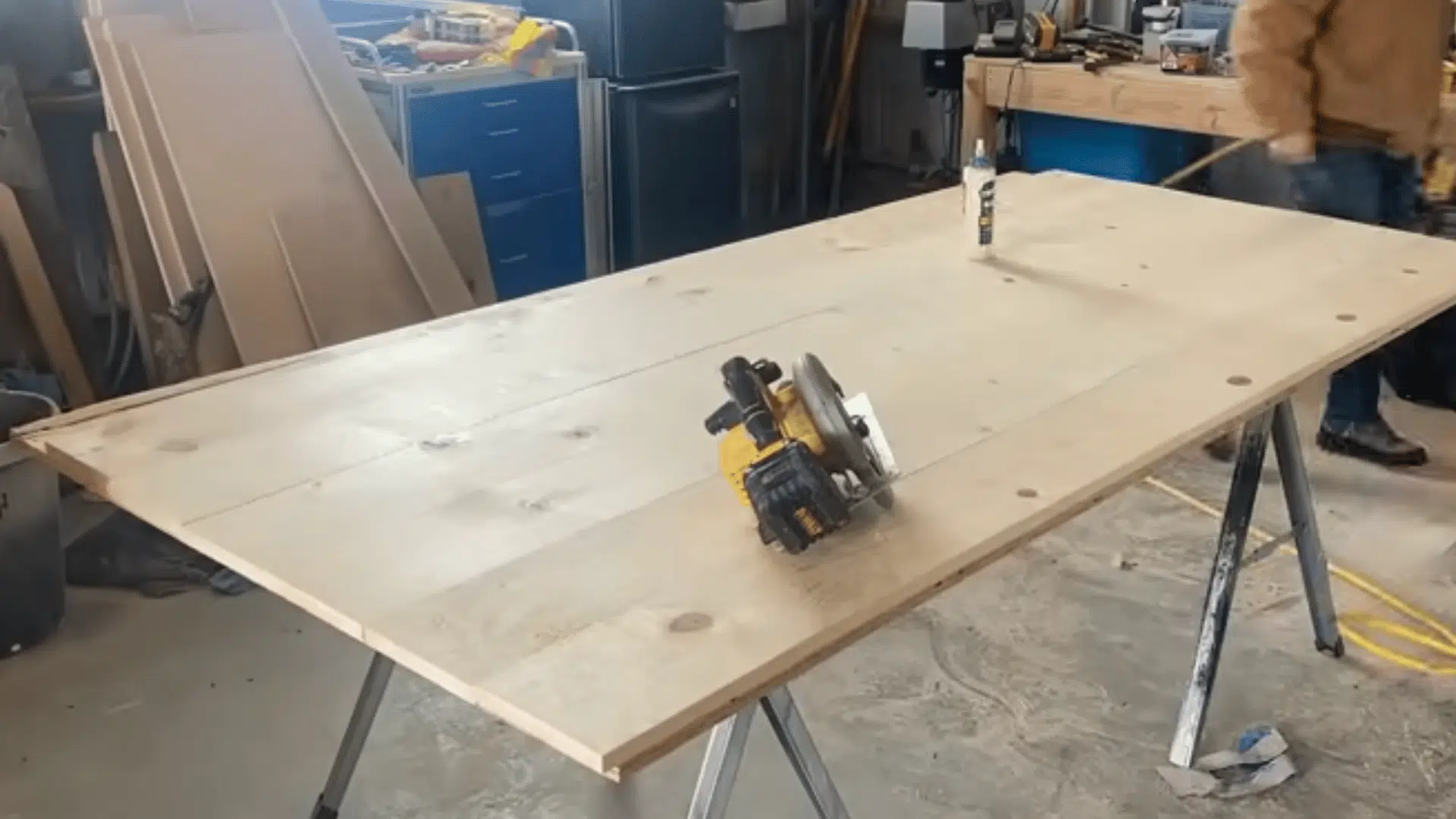 a large wooden tabletop assembled from wide planks resting on sawhorses inside a woodworking workshop