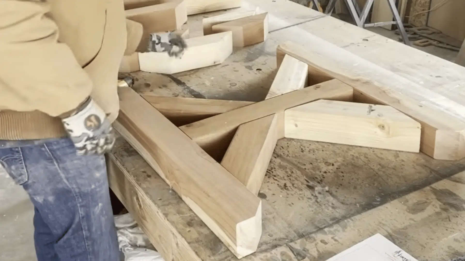 a woodworker arranging angled wooden supports and beams on a workbench preparing parts for table base assembly