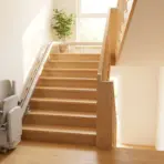 Stairlift beside wooden staircase in sunlit home interior with potted plant