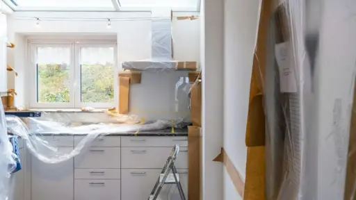 Kitchen under renovation covered in protective plastic with step ladder and natural light through window