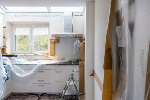 Kitchen under renovation covered in protective plastic with step ladder and natural light through window