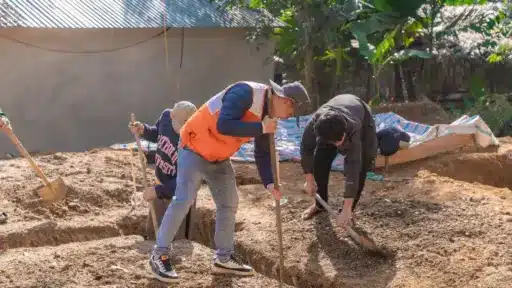 Construction workers digging soil trenches in an outdoor setting under bright sunlight