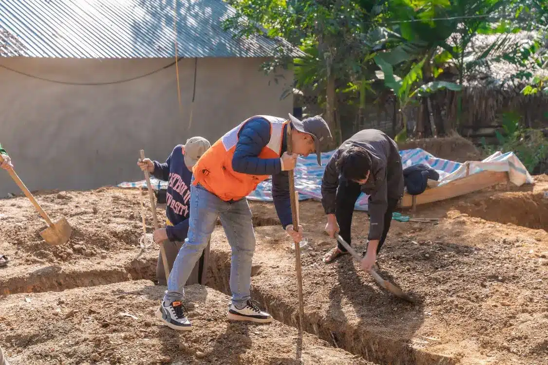 Construction workers digging soil trenches in an outdoor setting under bright sunlight