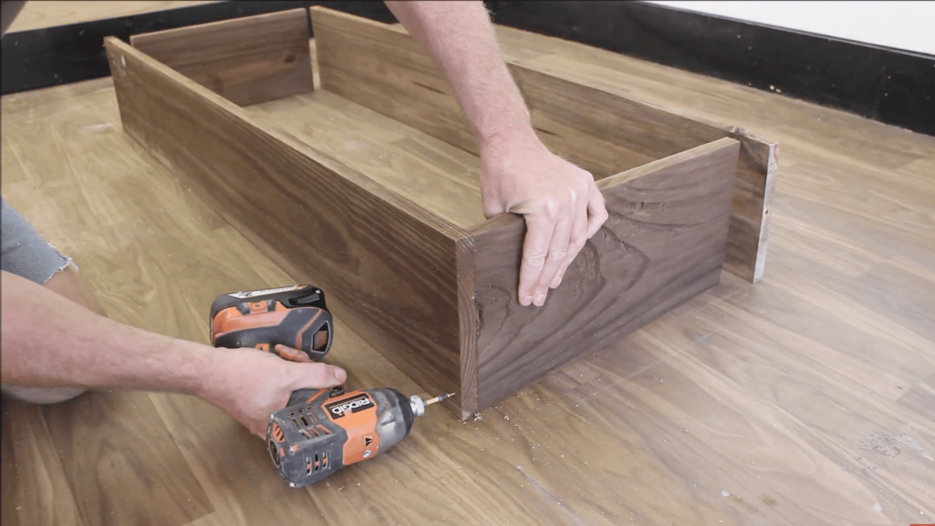 boards being affixed by screws and drill by a man's hand on a wooden furnished floor
