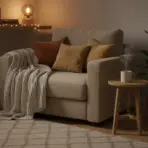 Cozy reading nook with beige armchair, knit blanket, warm pillows, and a steaming mug on side table