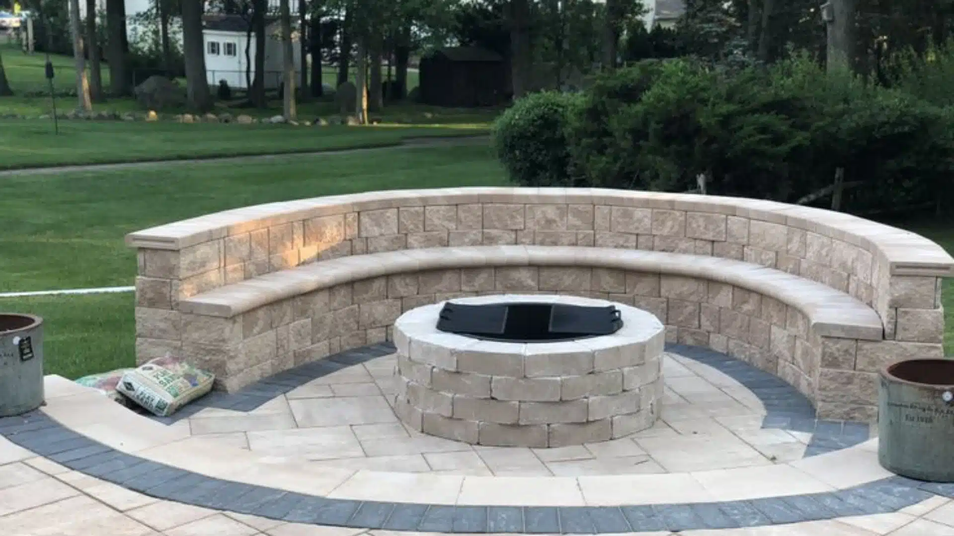 Curved backyard stone seating wall with built-in bench and circular DIY fire pit on a modern paved patio. (1)