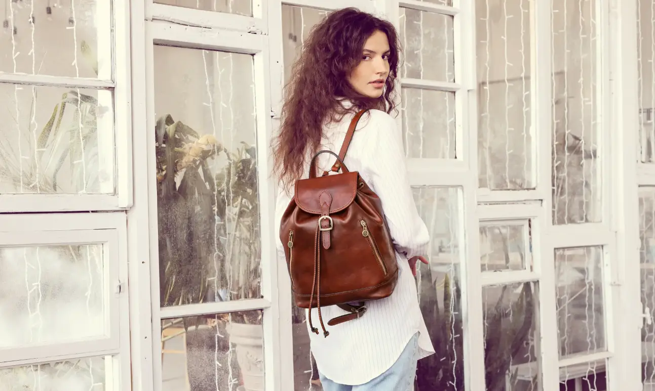 Woman with brown leather backpack standing in front of large windows indoors