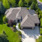 Suburban house with gray shingles and landscaped garden in lush green neighborhood