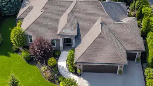 Suburban house with gray shingles and landscaped garden in lush green neighborhood