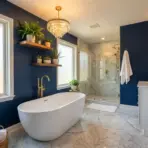 Luxurious bathroom with freestanding tub, marble floor, and navy walls adorned with gold fixtures