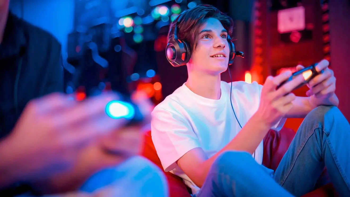 Young man wearing headphones playing video game in dimly lit room with blue and red lighting