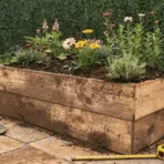 freshly built wooden diy planter box on a sunny patio filled with bright flowers and green herbs