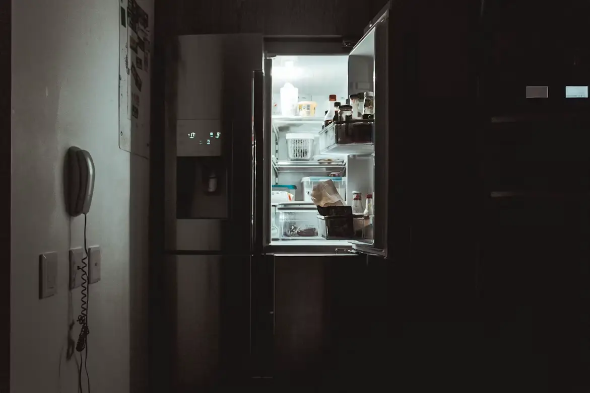 Open refrigerator with assorted items inside in dimly lit kitchen setting