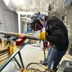Welder in protective gear working on metal pipe in industrial workshop setting