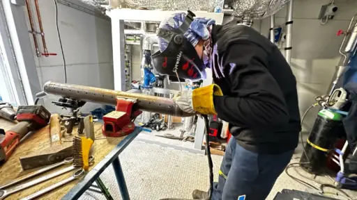 Welder in protective gear working on metal pipe in industrial workshop setting