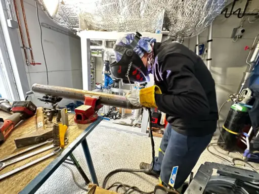 Welder in protective gear working on metal pipe in industrial workshop setting