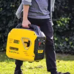 Person carrying yellow portable generator outdoors on grass with greenery background
