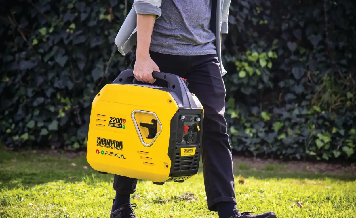 Person carrying yellow portable generator outdoors on grass with greenery background