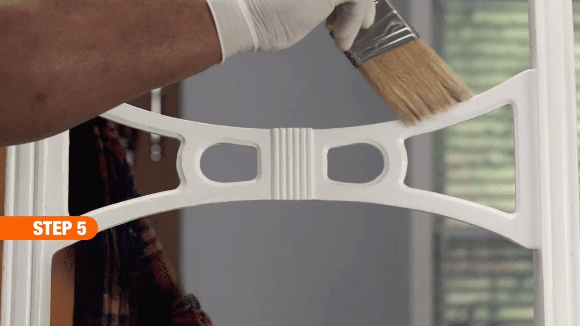 gloved hand brushing a clear sealant onto a painted wooden chair backrest to protect and finish the restored surface