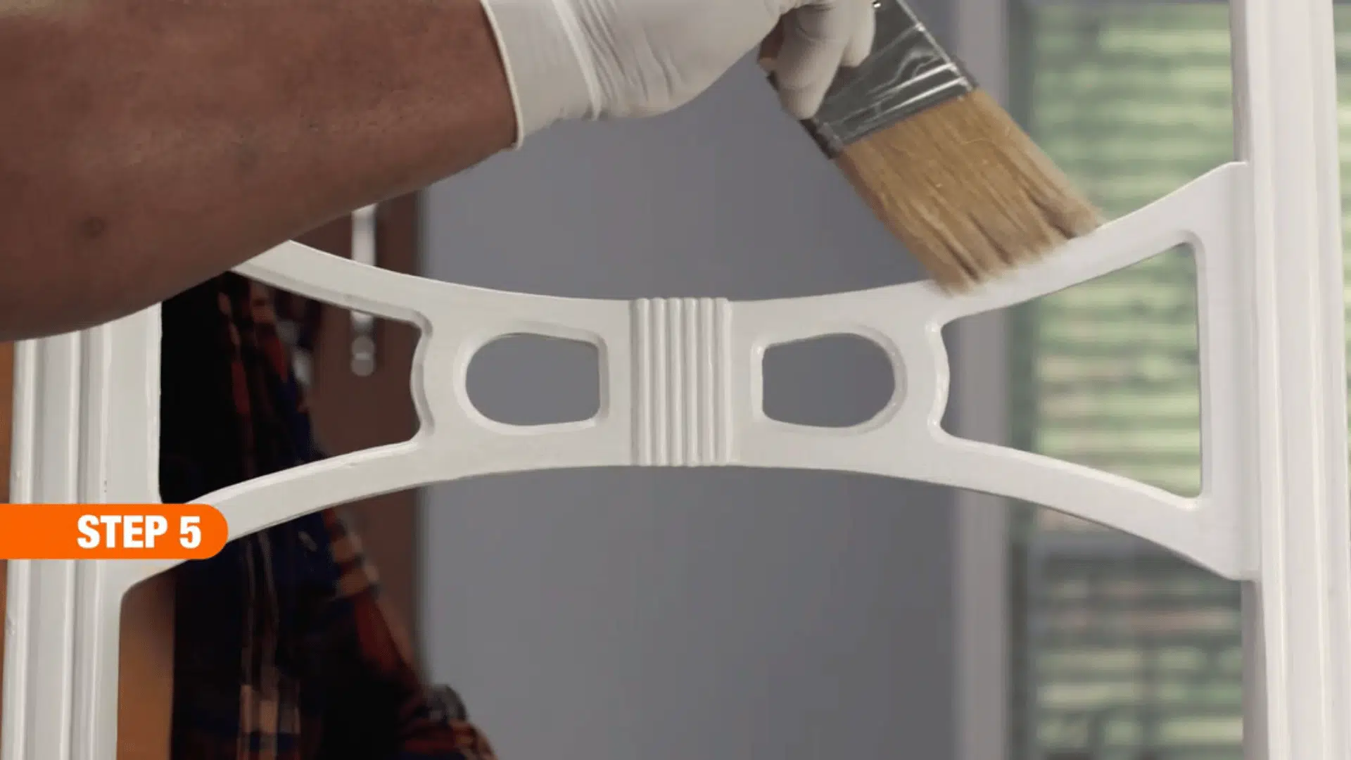 gloved hand brushing a clear sealant onto a painted wooden chair backrest to protect and finish the restored surface