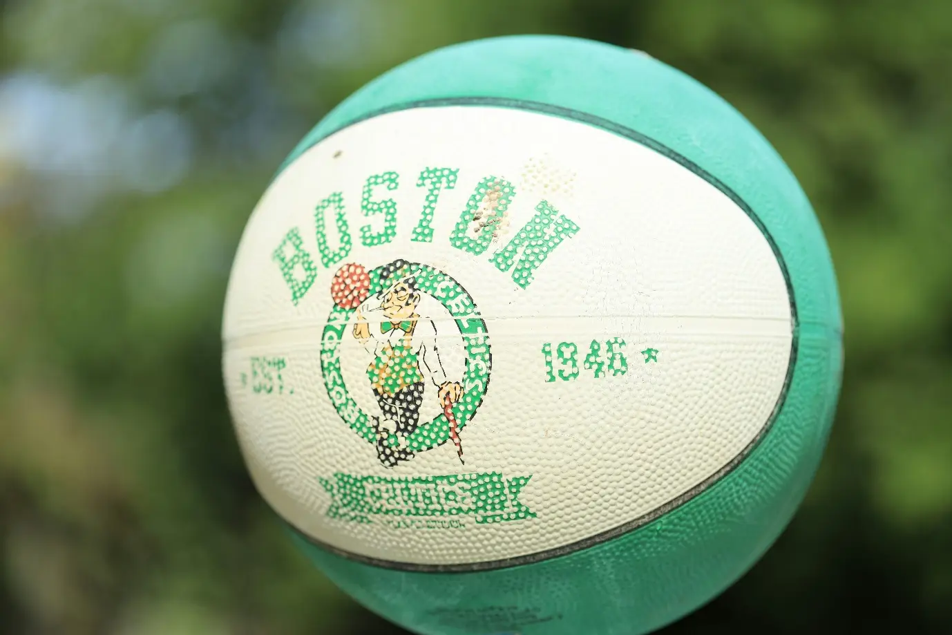 Green and white basketball with Boston logo against blurry outdoor background