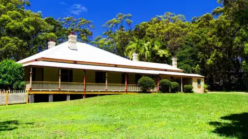 Traditional wooden house with white roof surrounded by lush greenery under clear blue sky