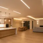 Modern open-plan kitchen and living area with wooden floors, pendant lighting, and minimalist furniture