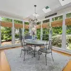 Elegant dining room with glass table, wrought iron chairs, surrounded by large windows and greenery