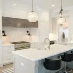 Modern white kitchen with marble backsplash, pendant lighting, and stainless steel appliances
