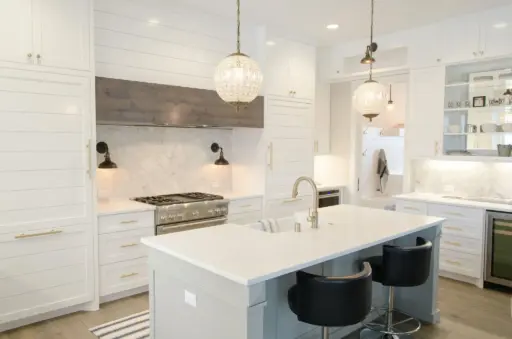 Modern white kitchen with marble backsplash, pendant lighting, and stainless steel appliances