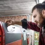Man adjusting control panel on red industrial machine in brick-walled workshop